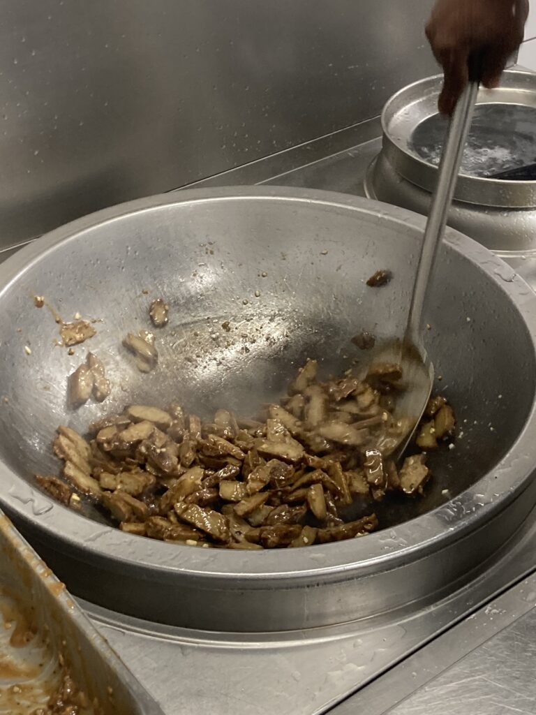 Le cuisinier du restaurant « Les Bons Enfants Végétarien » mélange à haute température de l'ail avec de la viande végétale à base de farine, de sel et d'eau pour préparer un civet végétarien.